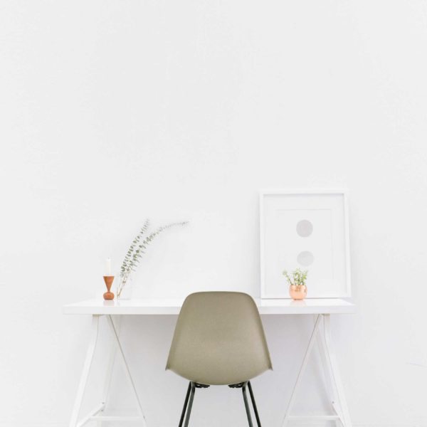 Minimalist office space featuring a white desk, chair, and art.
