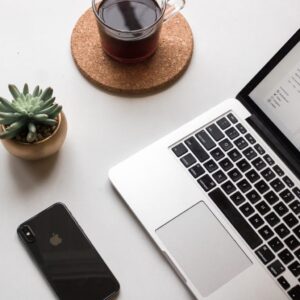 Overhead view of an open laptop, coffee, smartphone, and potted plant on a desk.