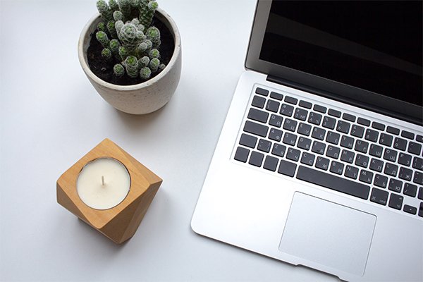 Laptop, small cactus in a pot, and a candle arranged neatly on a clean white desk.
