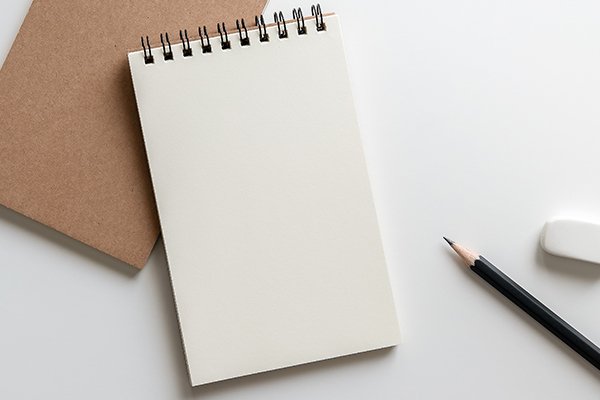 Spiral notebook, pencil, eraser, and brown folder neatly arranged on a plain white surface.